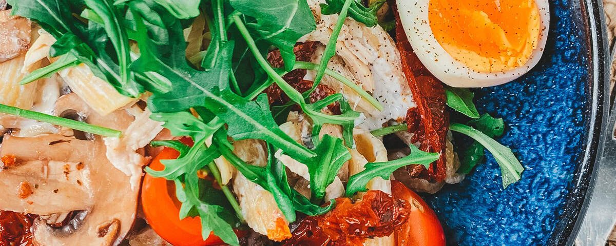 Truffelpasta met pulled chicken en champignons, rucola en half gekookt eitje in een kom – romig en hartig.