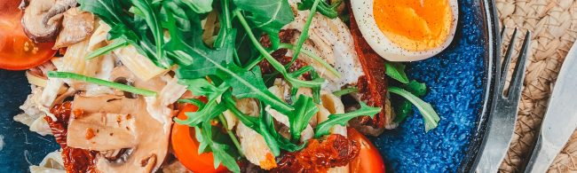 Truffelpasta met pulled chicken en champignons, rucola en half gekookt eitje in een kom – romig en hartig.