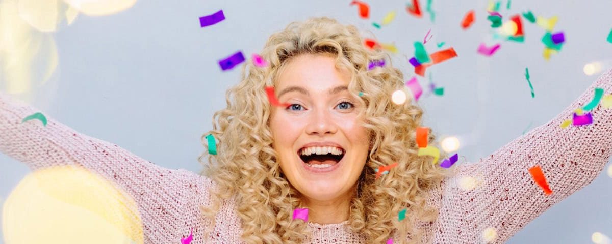 Vrouw juicht met vallende confetti — nieuwjaar en goede voornemens, feestelijke start van gezonde doelen.