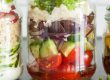 Mexicaanse salade in een pot (jar) met kleurrijke lagen van bonen, paprika, avocado, maïs en couscous—handig en voedzaam.