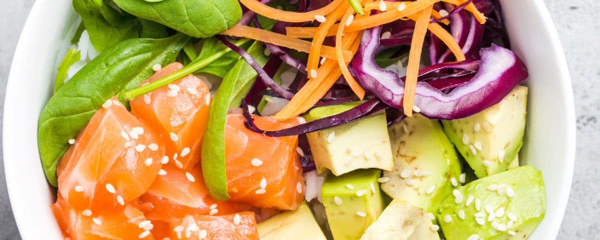 Home made poké bowl met gerookte zalm, avocado, spinazie, wortel, rode kool en dressing van sojasaus, sesamolie en rijstazijn—garnering met sesamzaadjes.