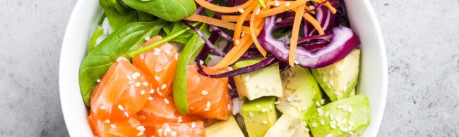 Home made poké bowl met gerookte zalm, avocado, spinazie, wortel, rode kool en dressing van sojasaus, sesamolie en rijstazijn—garnering met sesamzaadjes.