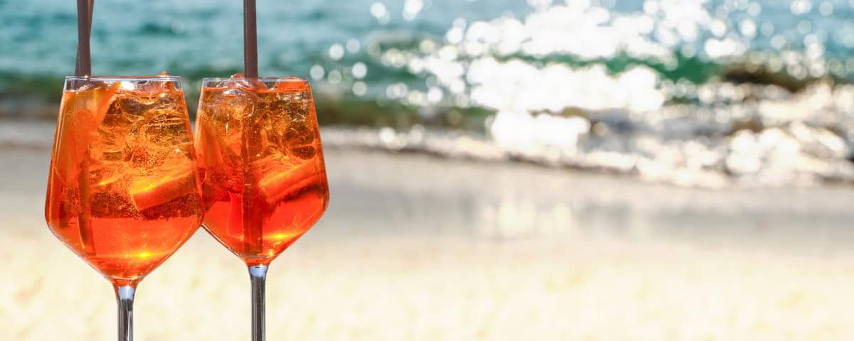 Alcoholvrije Aperol-stijl spritz met sinaasappel, granaatappel en bruiswater in wijnglas met ijs, sinaasappelschijf en rozemarijn.