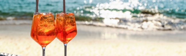 Alcoholvrije Aperol-stijl spritz met sinaasappel, granaatappel en bruiswater in wijnglas met ijs, sinaasappelschijf en rozemarijn.