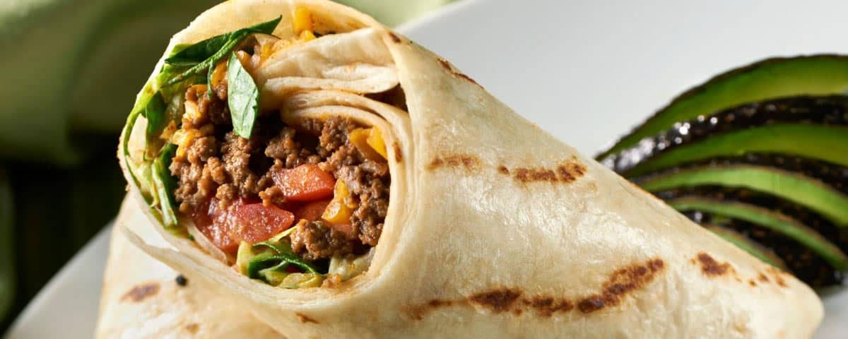 Gezonde fastfood wrap met mager rundergehakt, ijsbergsla, tomaat, augurk, ui en gesmolten kaas op volkoren wrap – gezonder alternatief voor een burger.